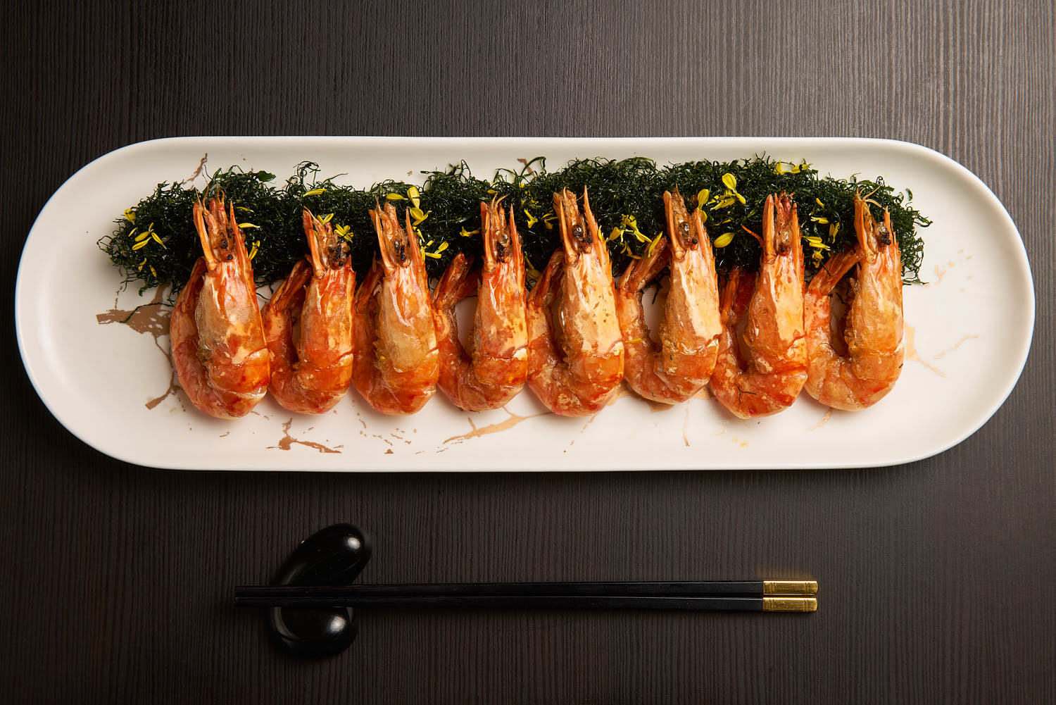 Top-down shot of a row of grilled prawns garnished with herbs and served on a white plate.