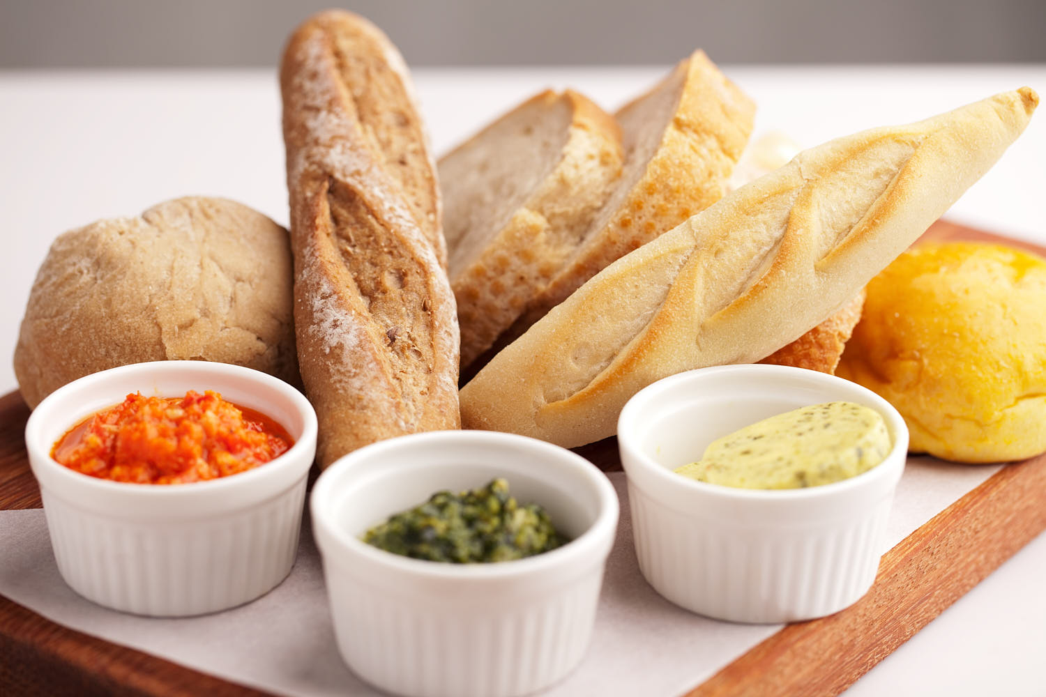 Assorted bread selection with butter and spices on a wooden serving board.