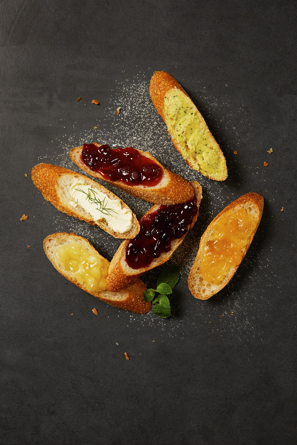 Soft baguette slices served with creamy cheese spreads, butter, jam, and honey and fresh herbs on a rustic plate.