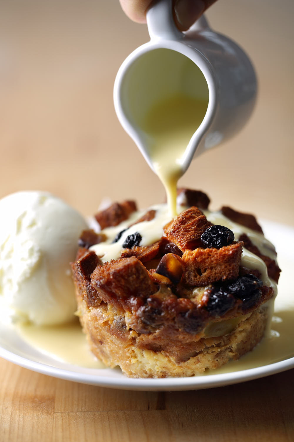 Bread pudding with a scoop of ice cream drizzled with vanilla sauce.