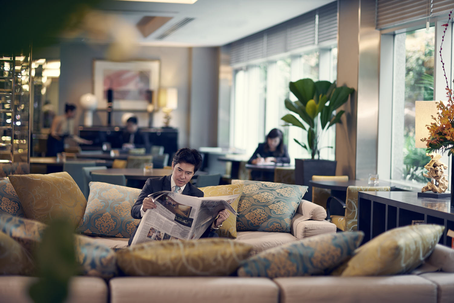 Businessman unwinding with a newspaper in a luxurious hotel lounge setting.