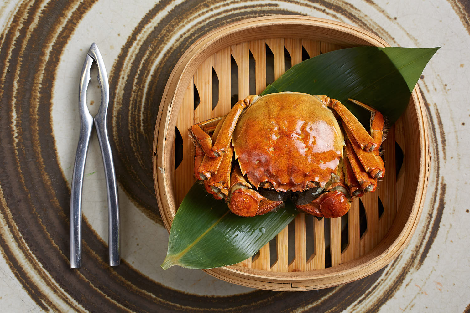 Gourmet hairy crab dish served on a minimalist bamboo steamer with artistic presentation.