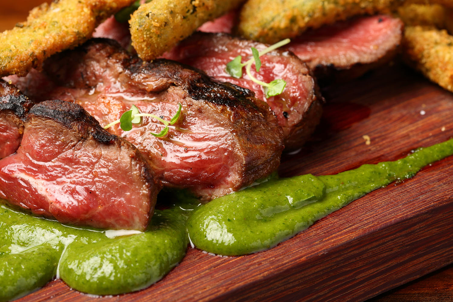 Close shot on medium rare beef slices with pesto dressing.