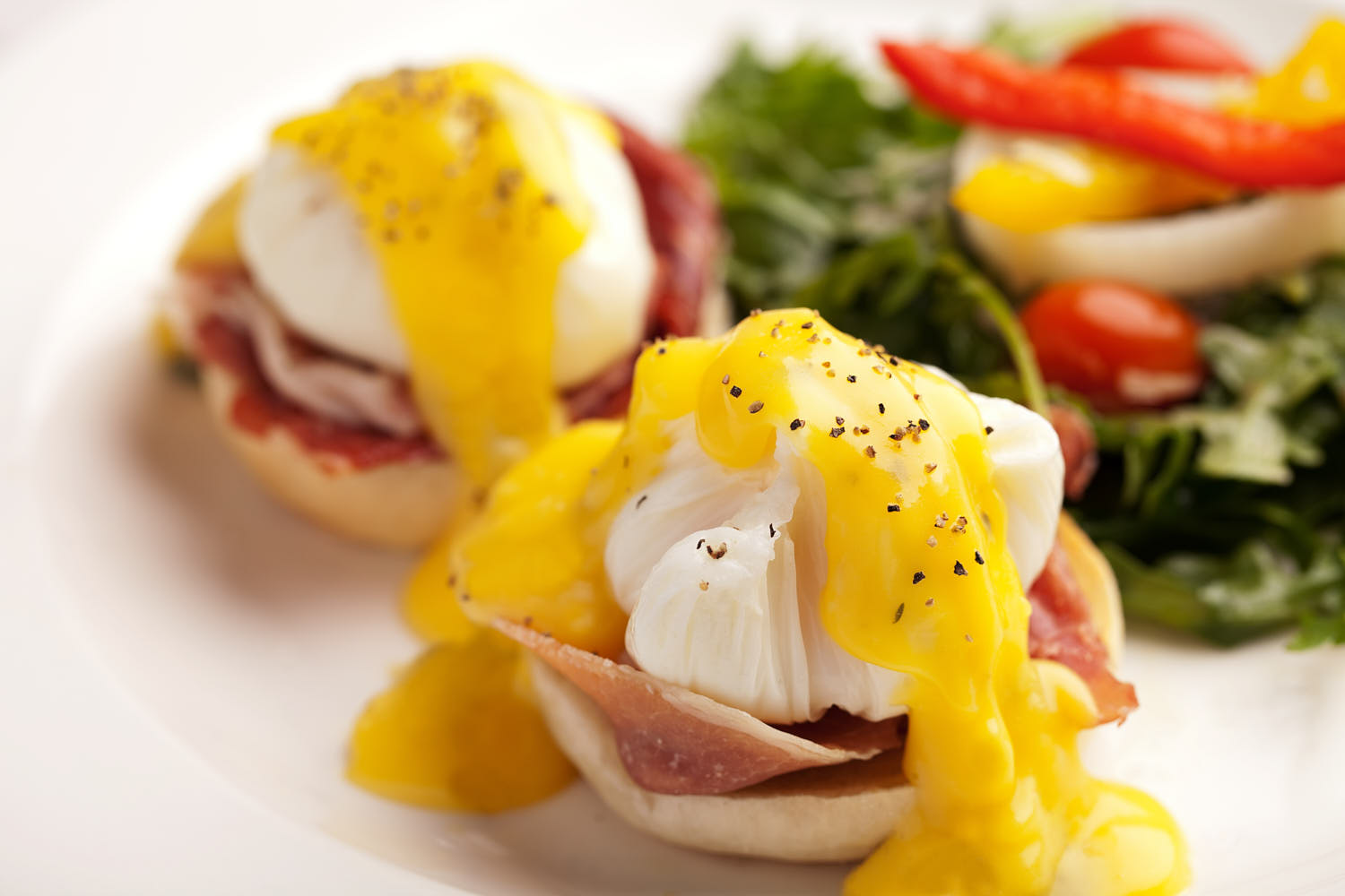 Classic egg benedict with poached eggs, ham, and salad with hollandaise sauce.