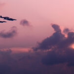 Fine art image of five F15 fighter planes flying in tight formation against an orange sunset over the Singapore skyline.