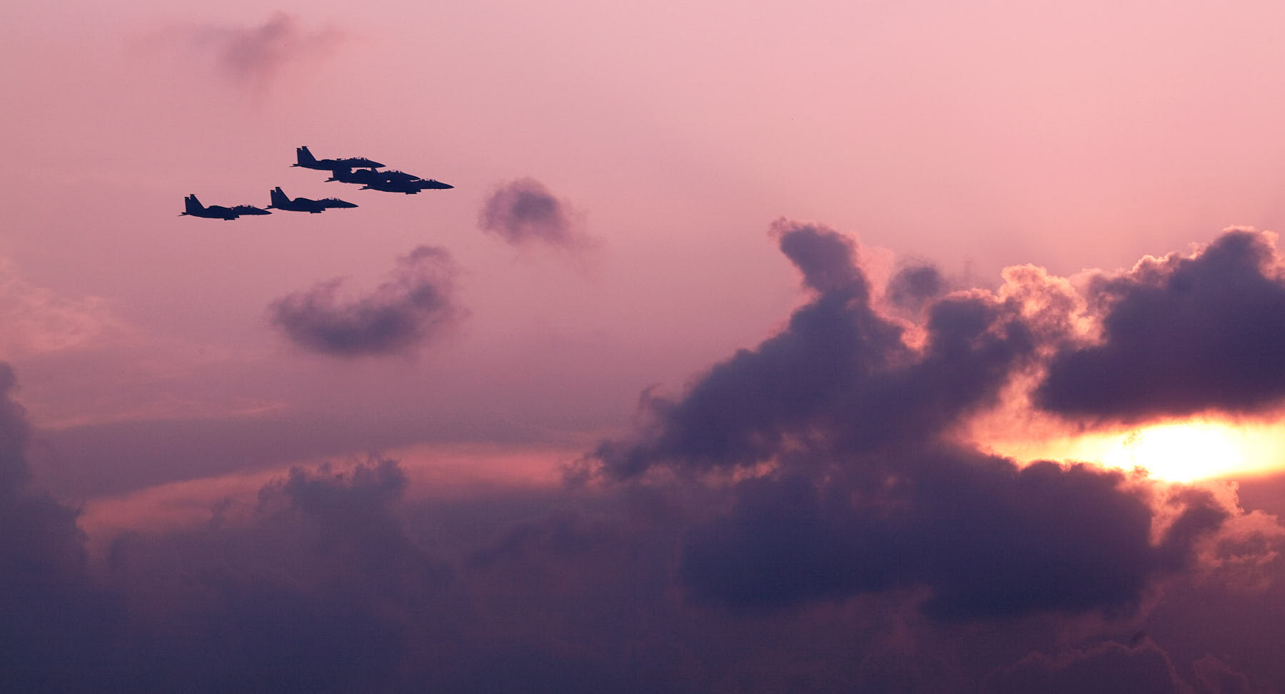 Fine art image of five F15 fighter planes flying in tight formation against an orange sunset over the Singapore skyline.