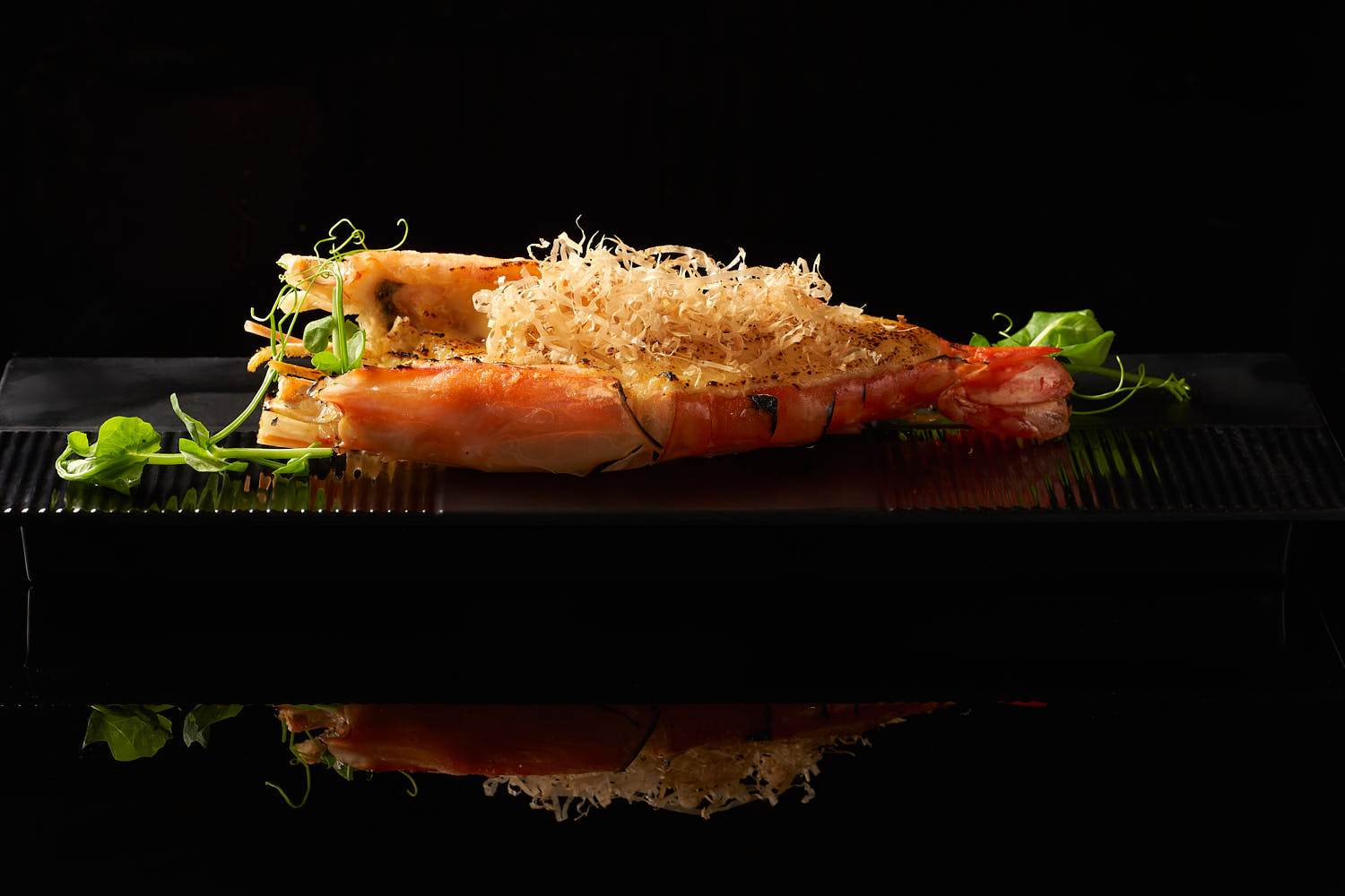 Grilled large prawn on a black fine dining plate.