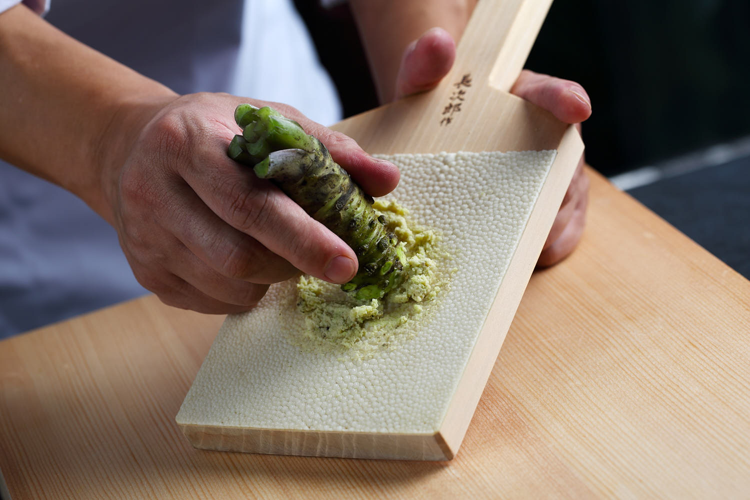 Chef grating fresh wasabi root with a traditional grater, preparing for sushi.