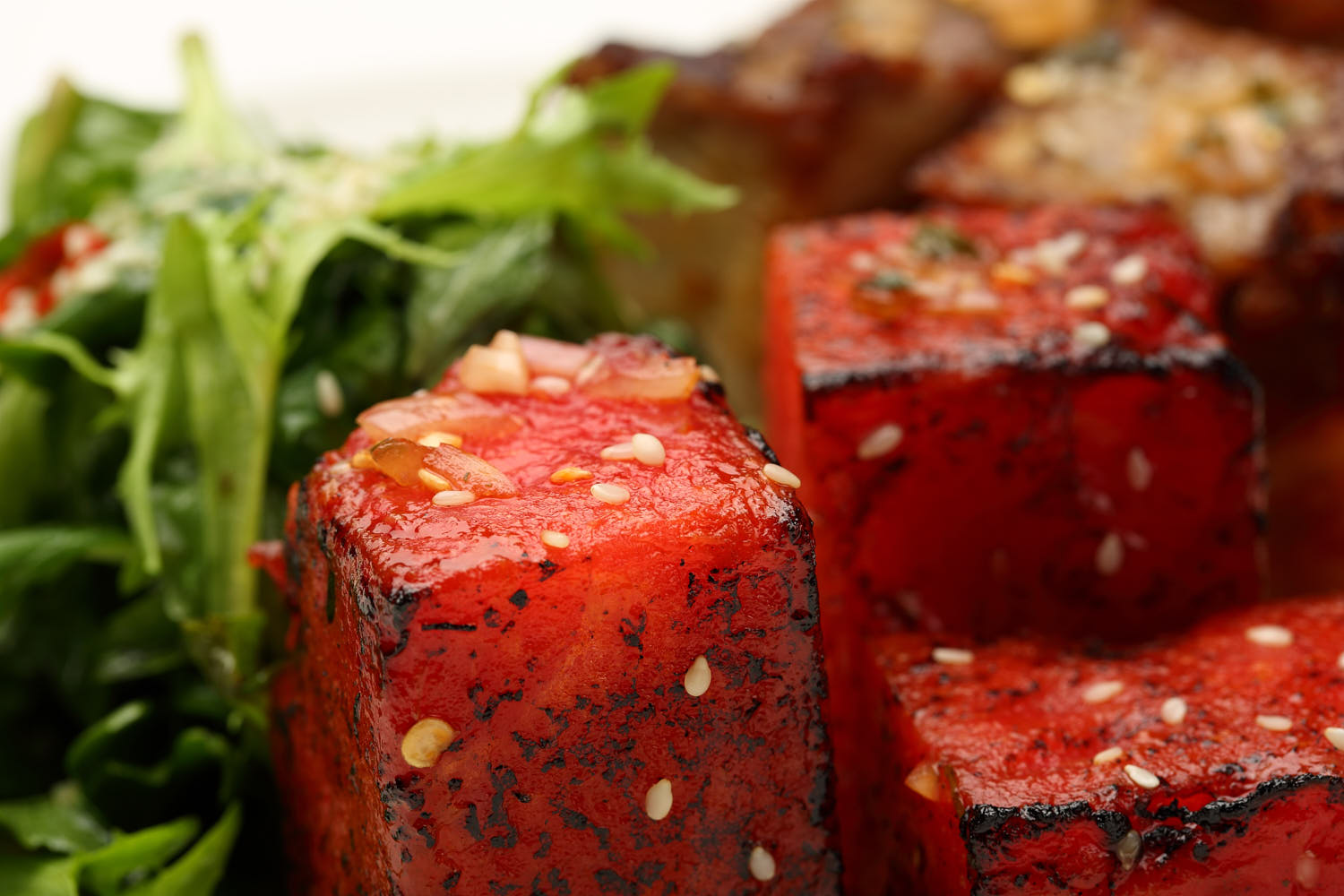 Grilled watermelon cubes with caramelized edges, served with a drizzle of sesame and fresh salad.