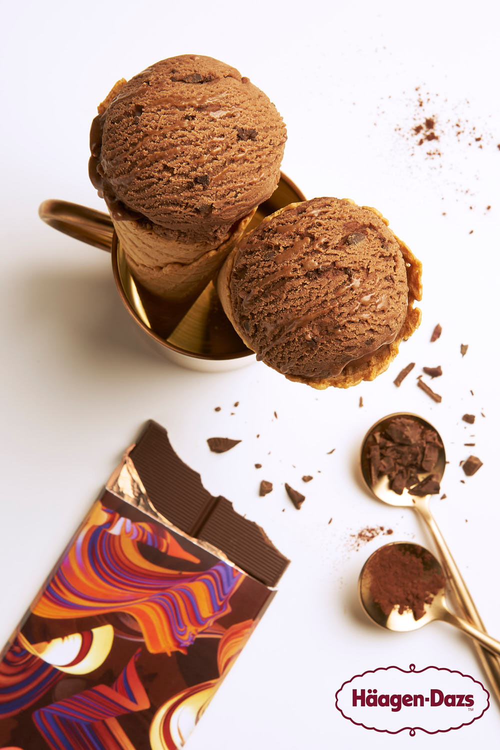 Häagen-Dazs Belgian chocolate ice cream on a cone styled with chocolate shavings, and gold dessert spoons.