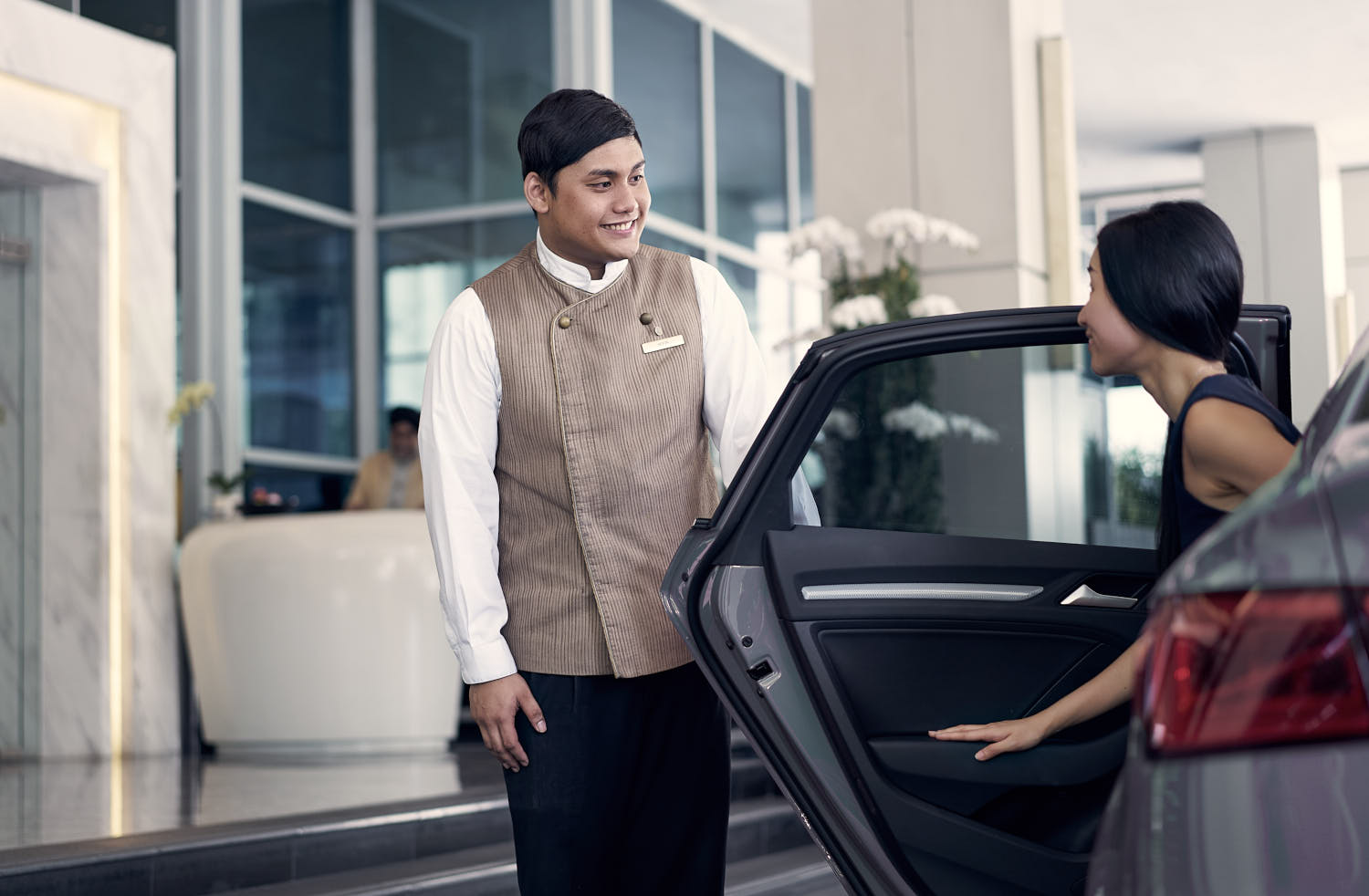 Hotel concierge opening the car door and warmly welcoming a guest to the hotel.