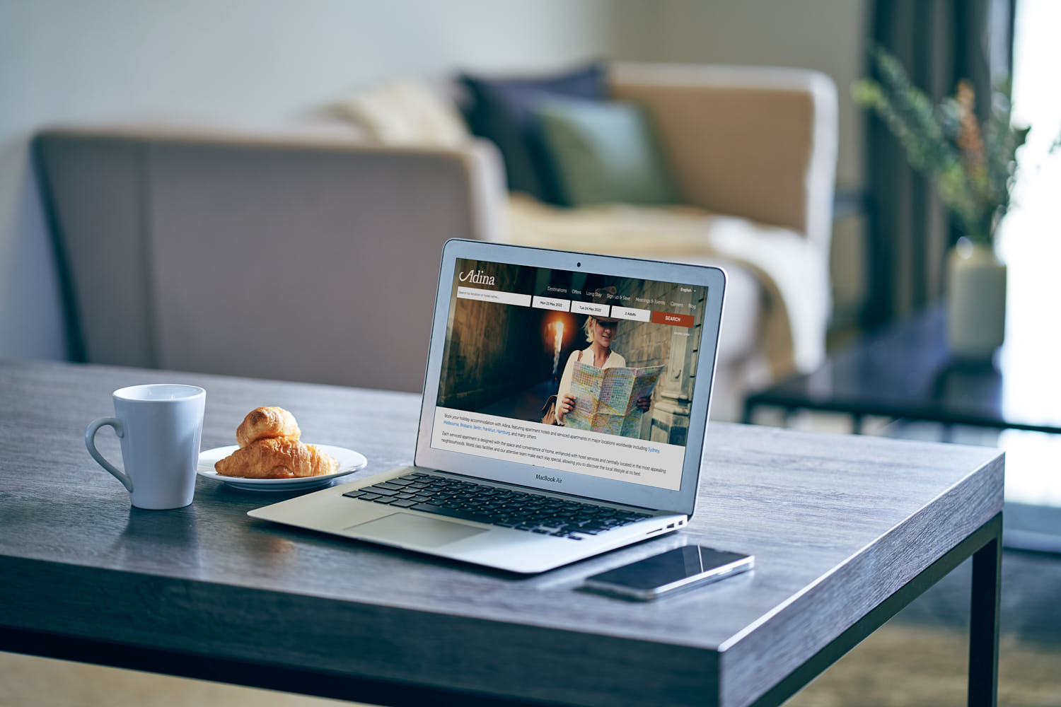Laptop, coffee cup, and croissant on a table inside a hotel room.