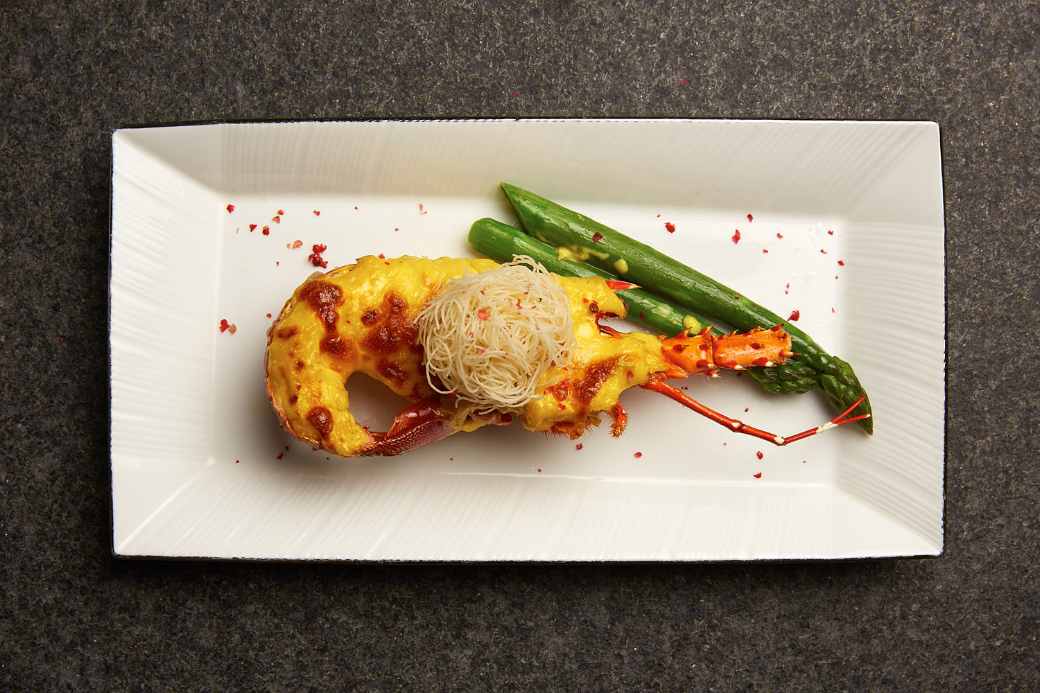 Top down shot of lobster grilled with cheese and asparagus.