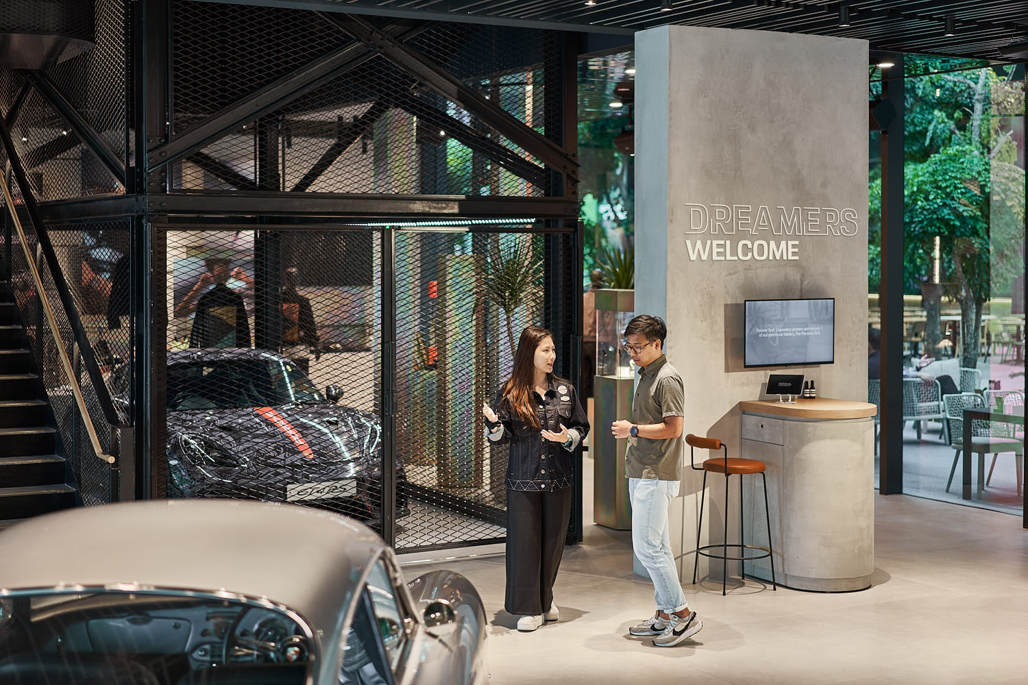 Luxury car sales executive welcoming a visitor at a Porsche studio.