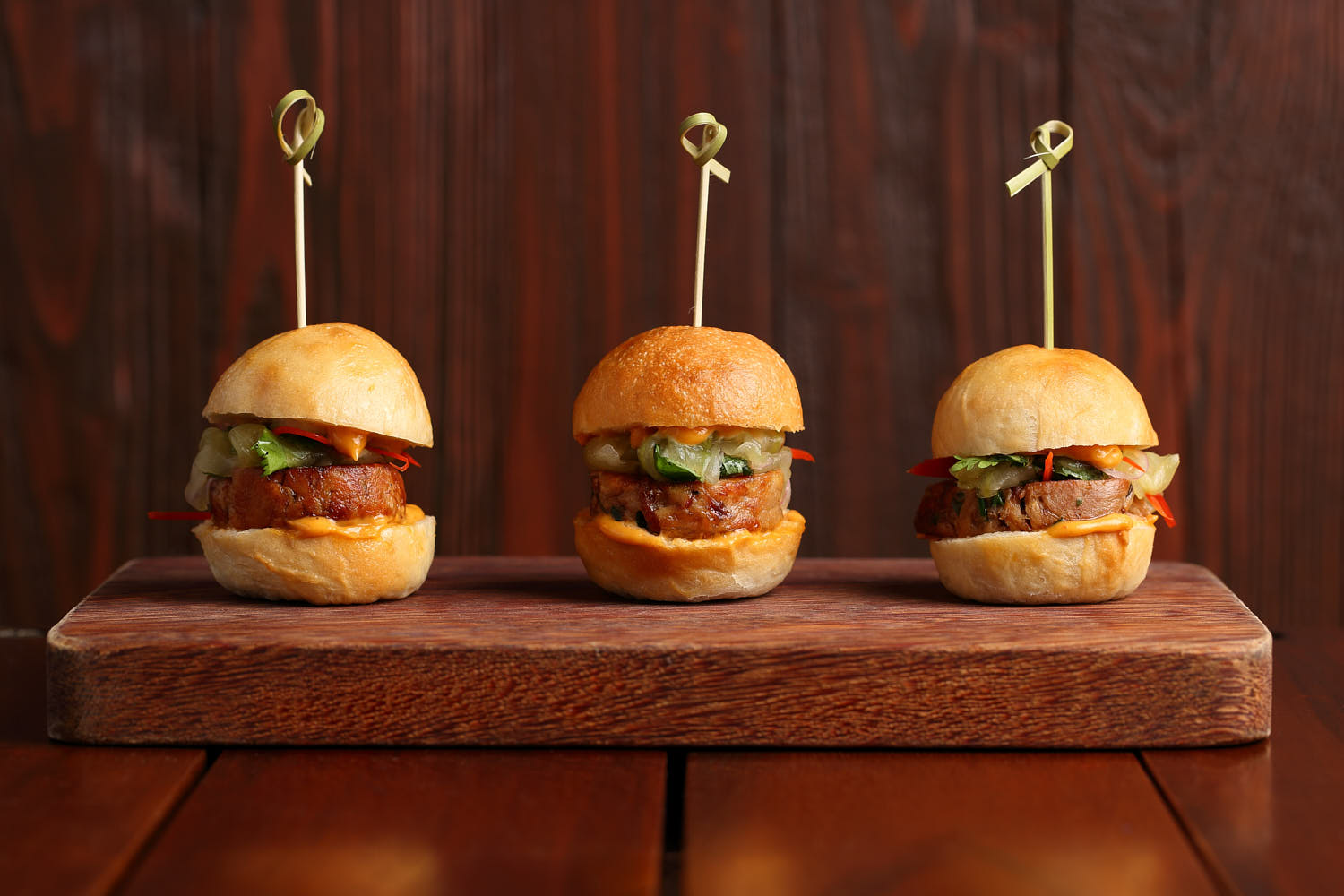 Three mini gourmet burgers with beef patties, cheese, and fresh toppings, served on artisan buns.