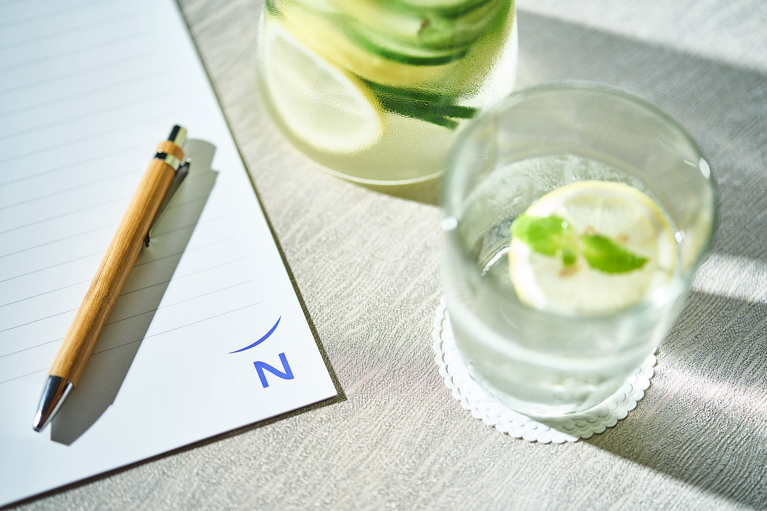 Top-down close-up of lemon and mint infused water with notepad and pen on table at Novotel.
