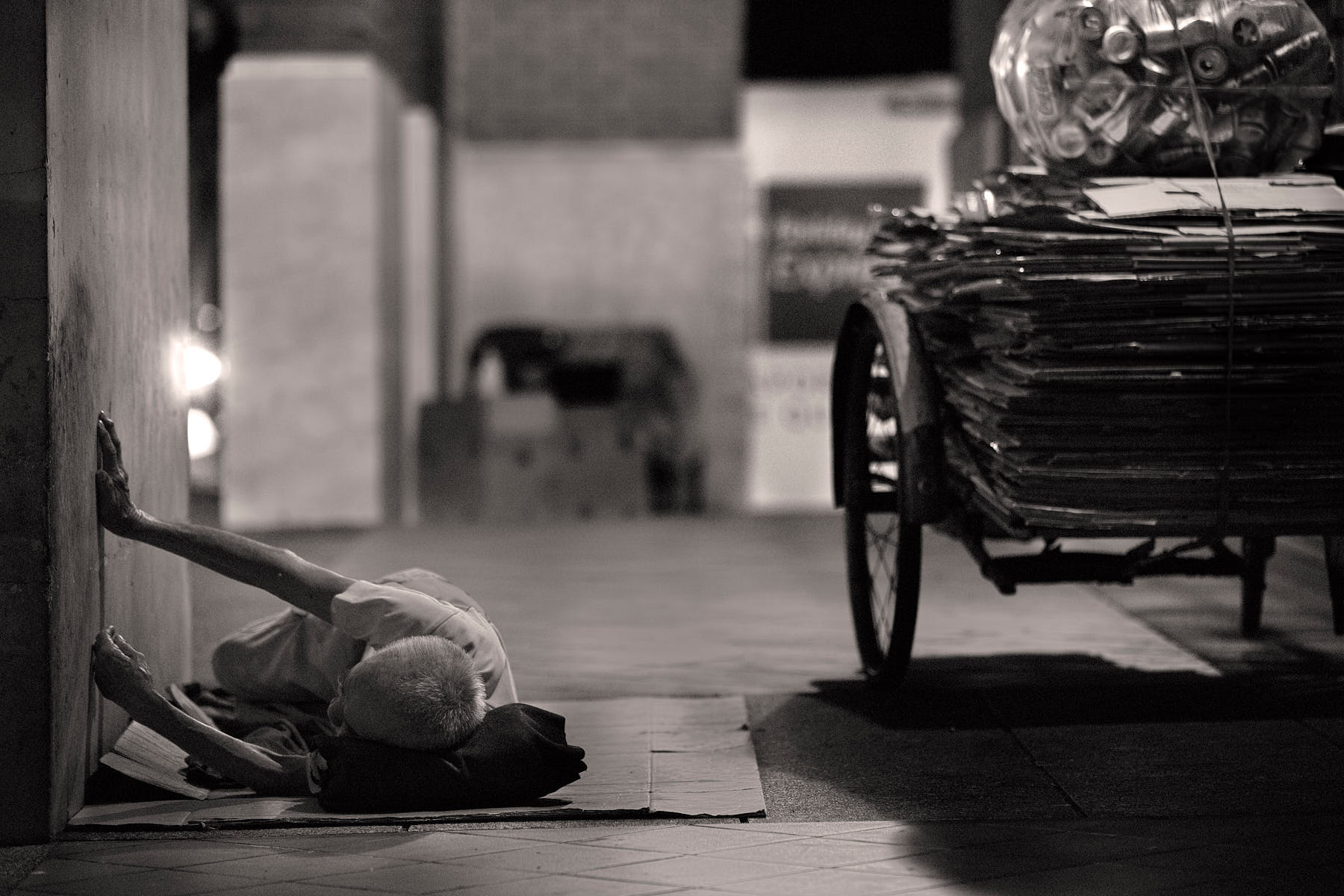 Old man resting on cardboard while collecting cardboard and cans in an alley at night in Clarke Quay, Singapore.