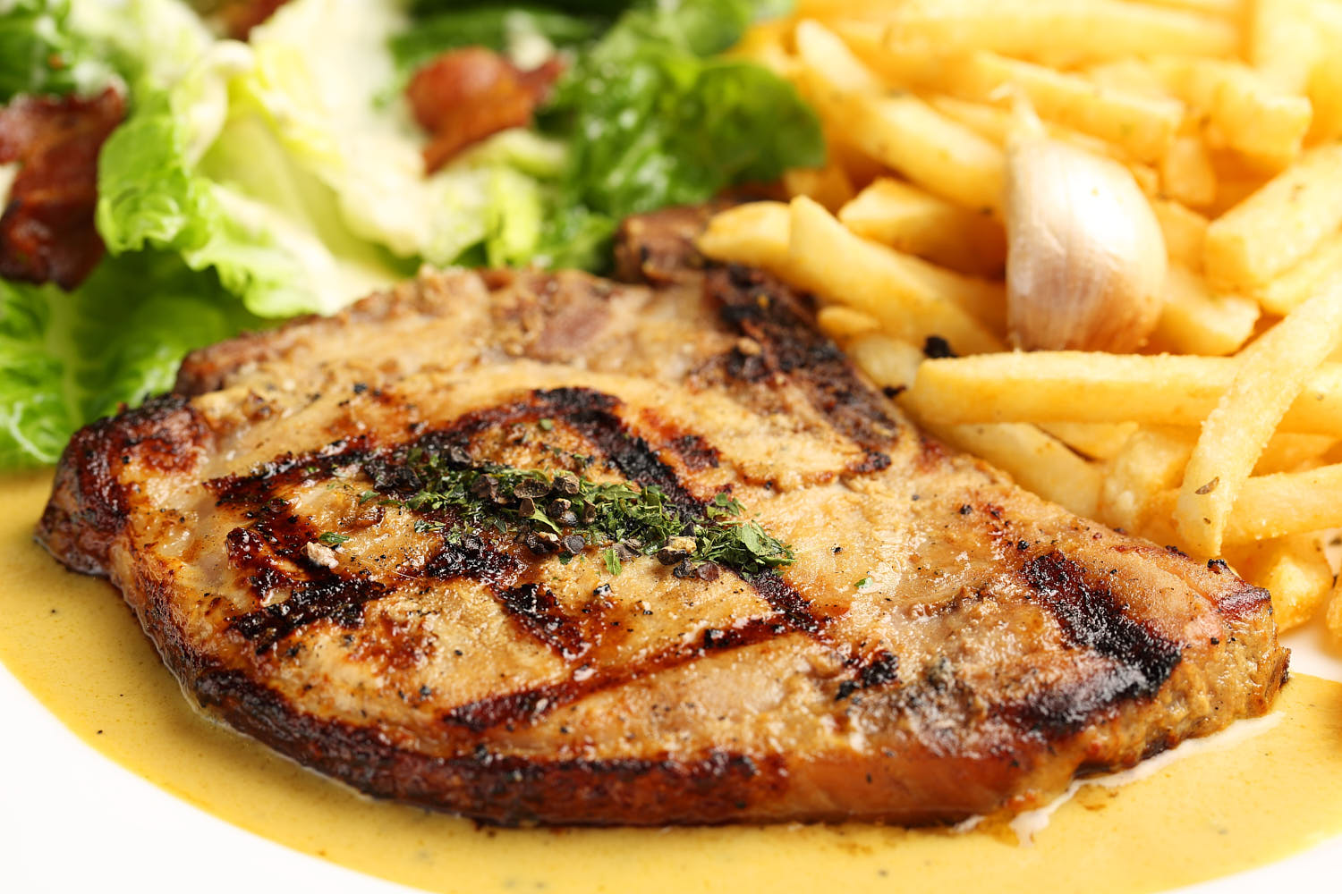 Close-up of grilled pork chop accompanied by a side of seasoned fries.