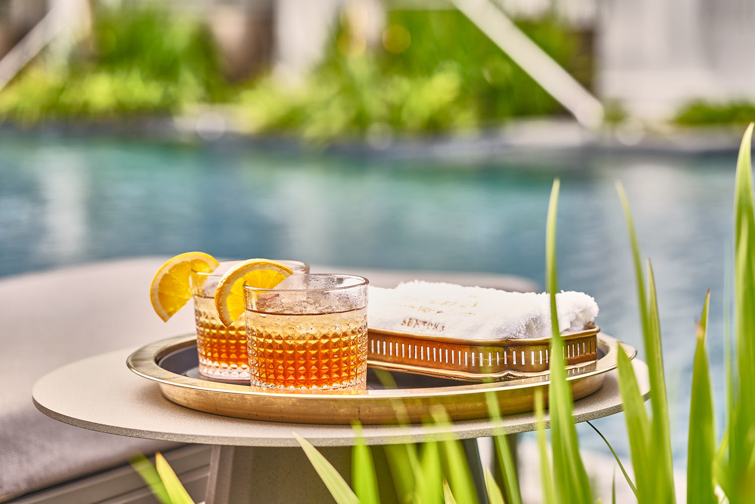 Two refreshment drinks and neatly folded towels at the poolside.