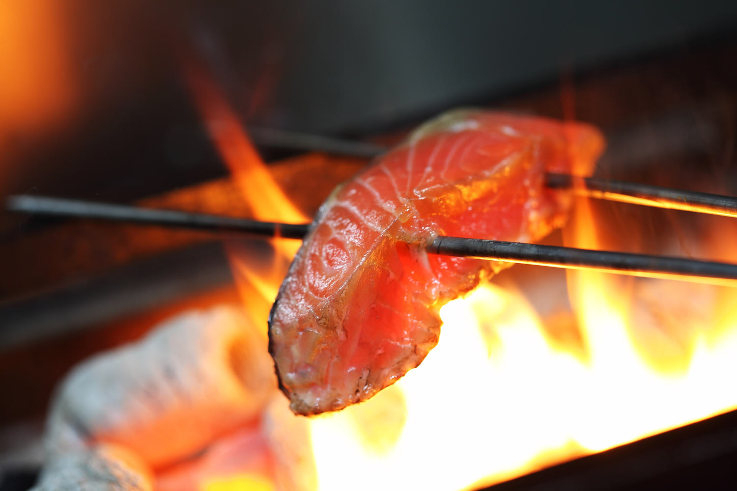 Close-up of salmon grilling over bright flames, showcasing sizzling texture.