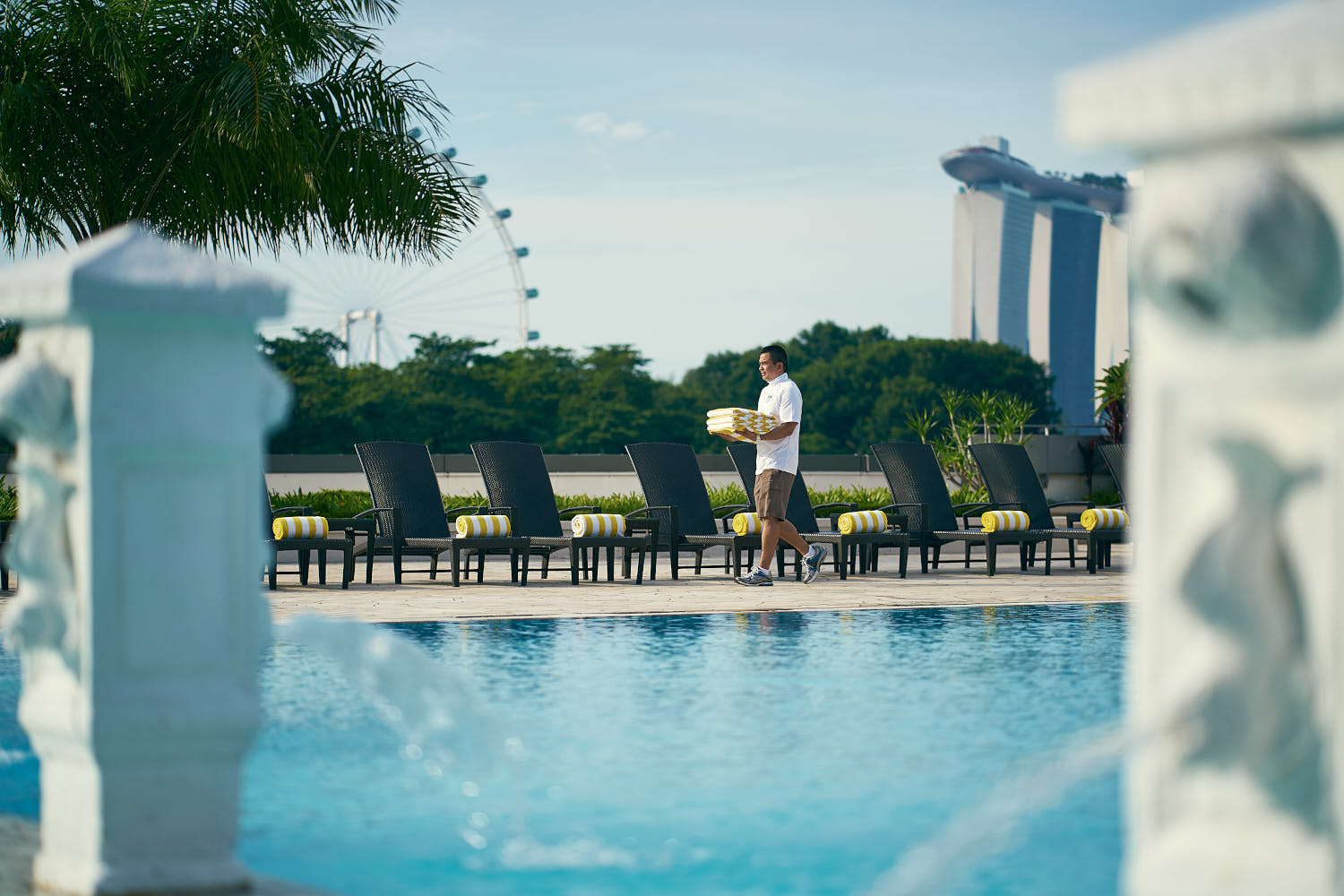 Hotel service staff setting up loungers and amenities around the resort pool.
