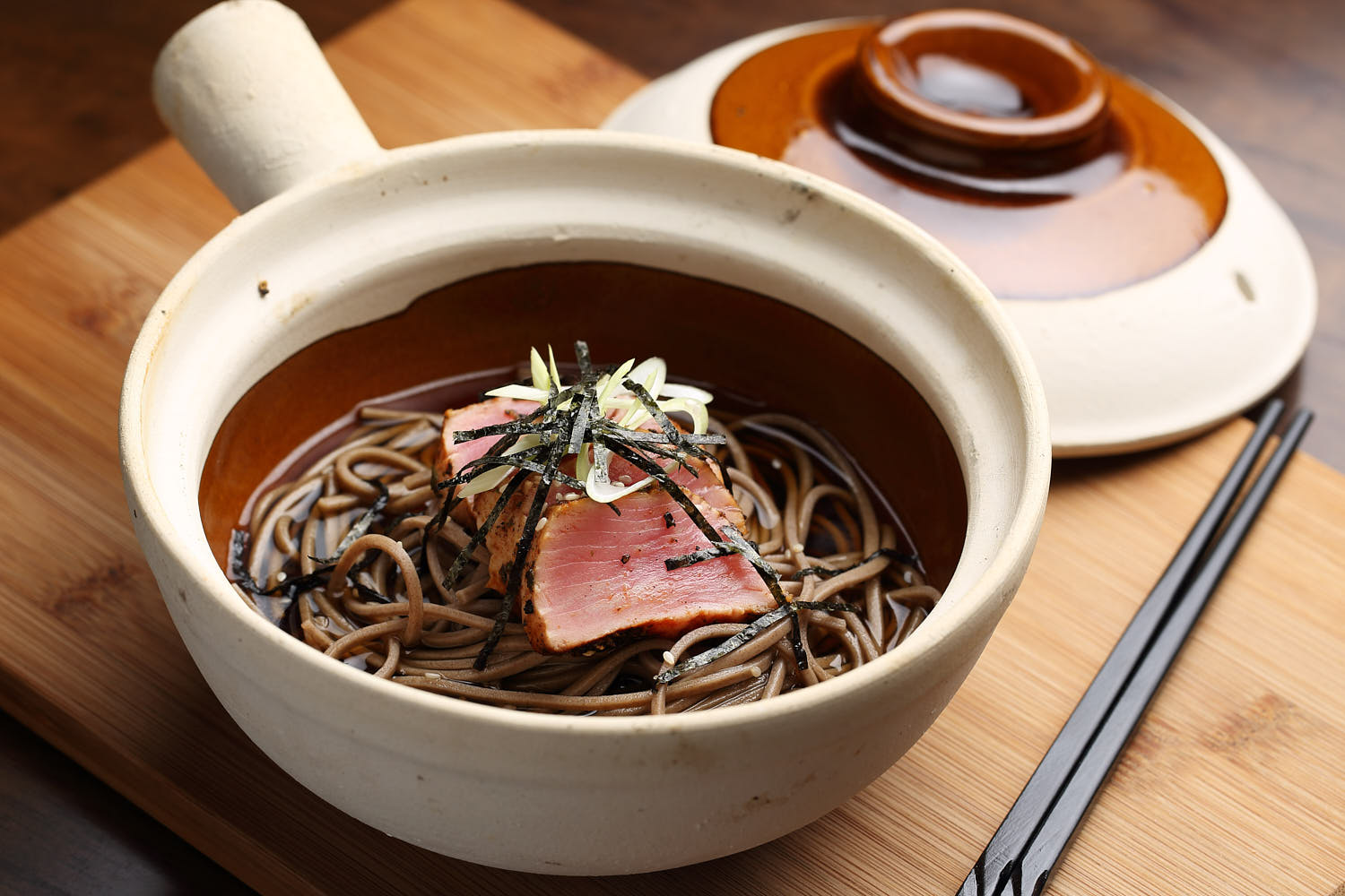 Claypot soba noodles with broth, served in a rustic Japanese ceramic bowl.