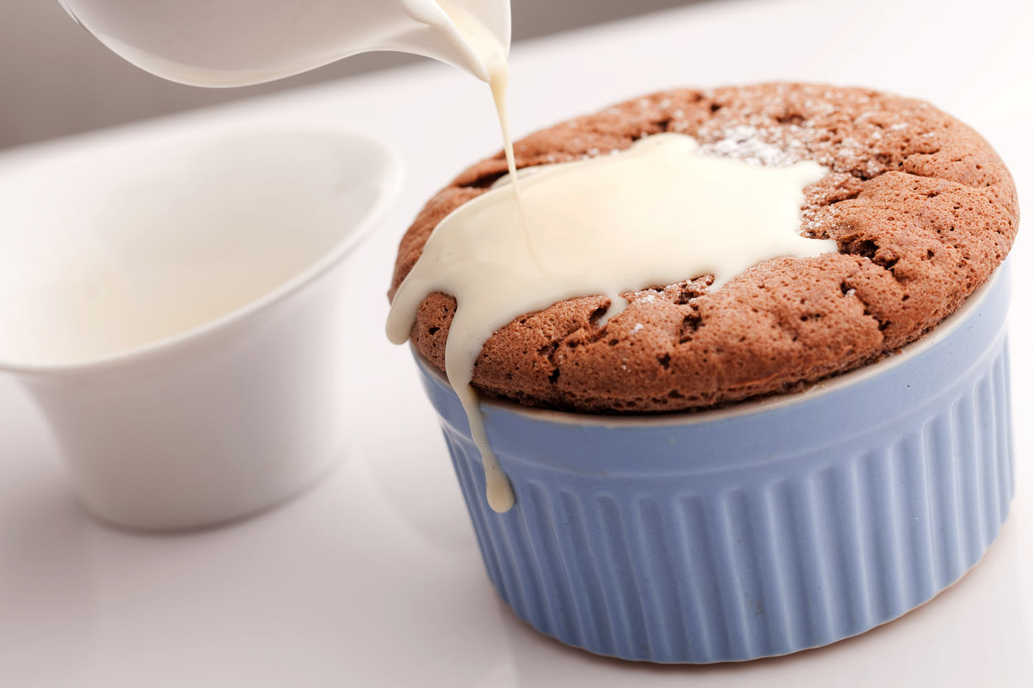 Close-up of creamy sauce being poured over a warm soufflé, capturing the motion.