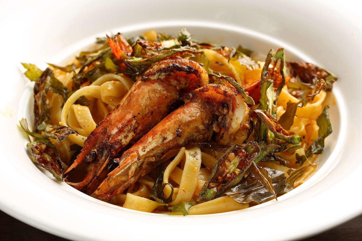 Close-up of creamy spicy prawn pasta topped with aromatic curry leaves.