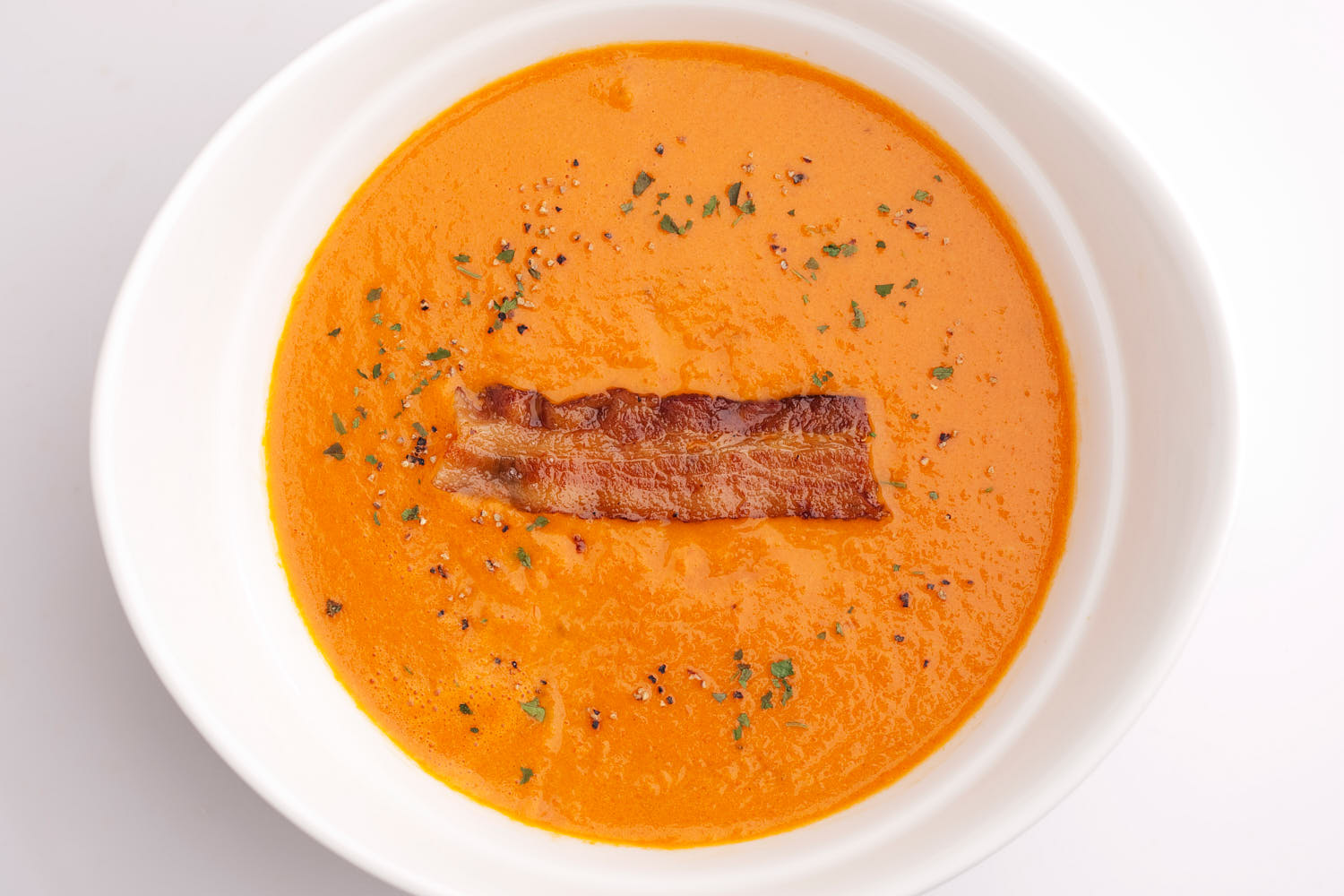 Close-up of rich tomato soup topped with crunchy bacon and fresh herbs.