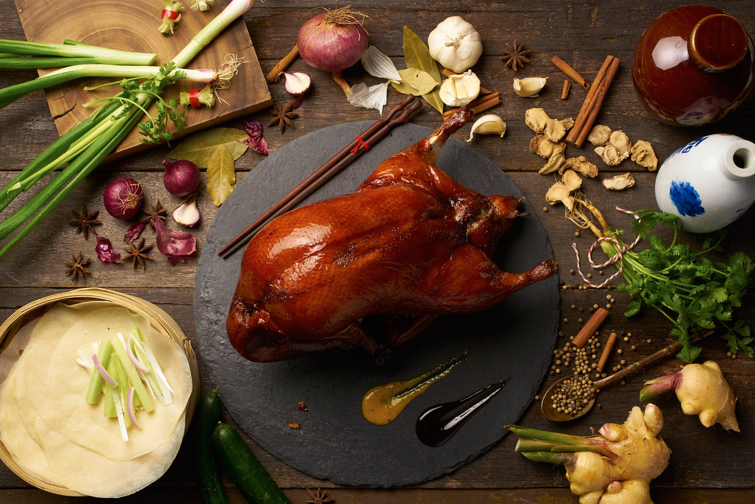 Whole Peking duck served on a rustic wooden table with traditional condiments in a lifestyle setting.