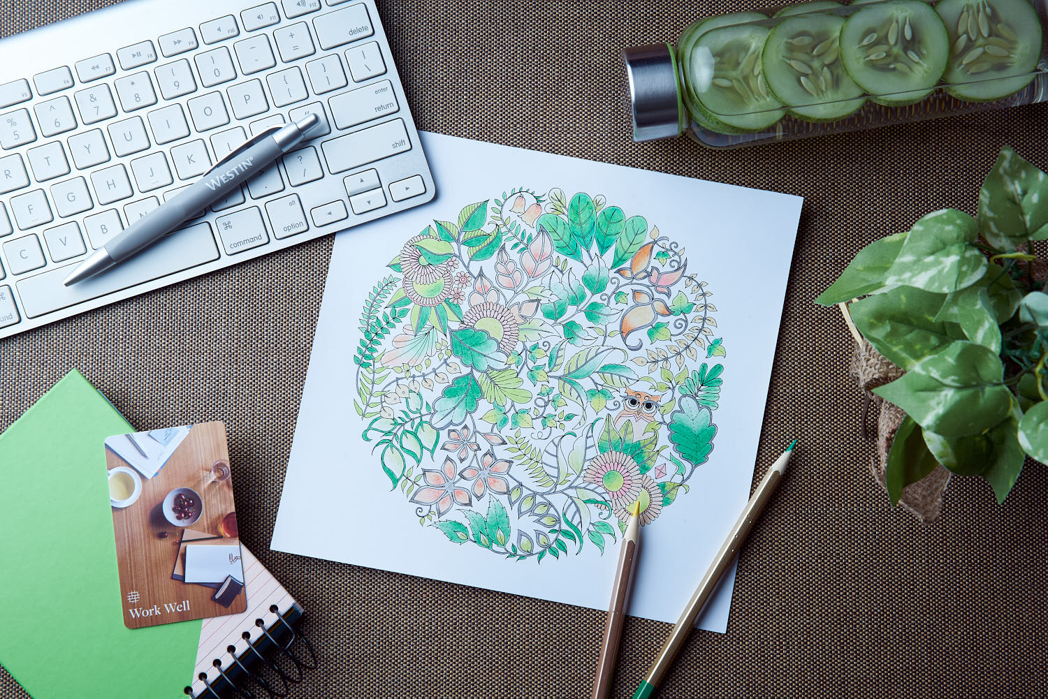 Refreshing cucumber cooler drink, colour pencil, keyboard, and plant on wooden table at Westin Hotel Johanna Basford collaboration.