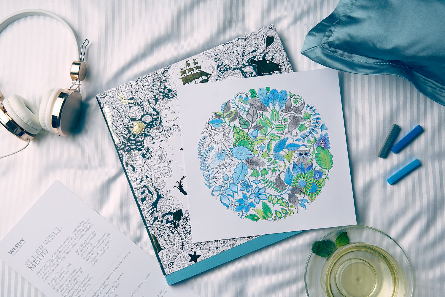 Close-up of headphone, crayon, pillow, and tea on a wooden surface at Westin Hotel Johanna Basford collaboration.