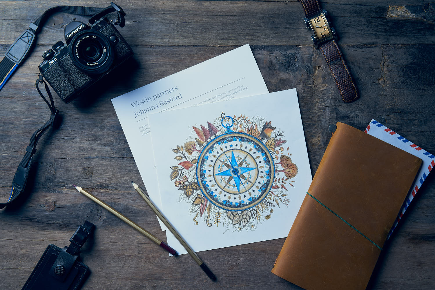 Wooden table top with camera, watch, and envelope at Westin Hotel collaboration with Johanna Basford.
